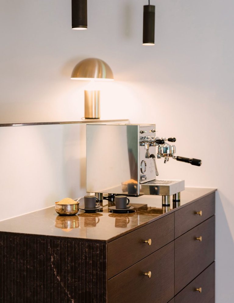 Moderne Kaffeebar mit Espressomaschine auf einem maßgefertigtem Schrank aus dunklem Holz mit brauner Marmorplatte und Messinggriffen