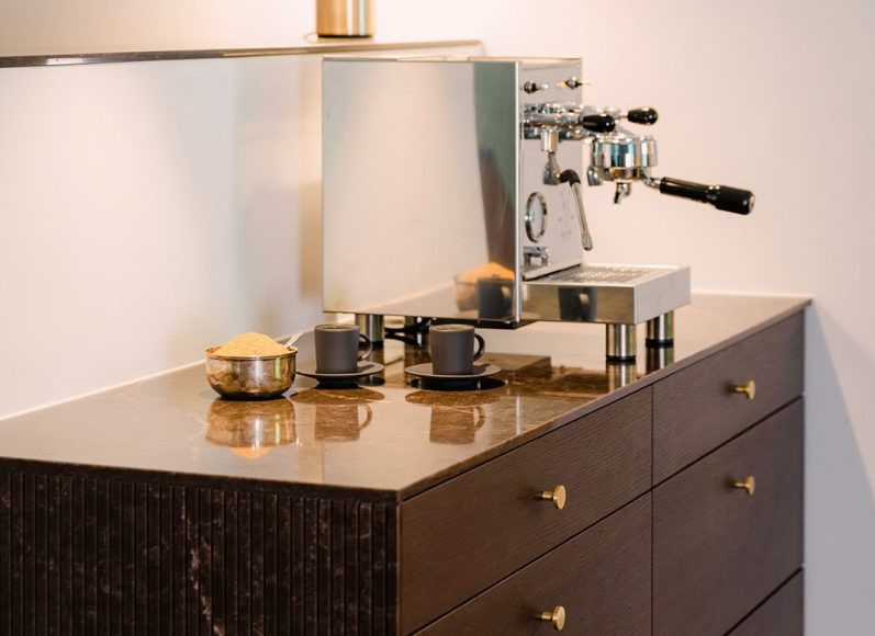 Hochwertige Espressomaschine auf einem maßgefertigten kaffebraunen Holzschrank mit Maromorplatte und runden Messinggriffen